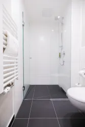 Ein modernes Badezimmer mit einer Dusche und schwarzen Fliesen. Die Wände sind in Weiß gehalten, und ein Handtuchhalter ist sichtbar.