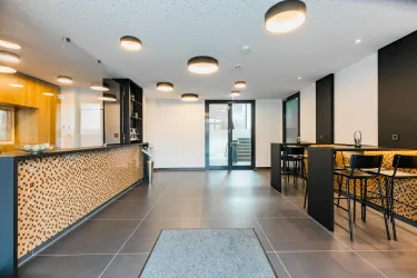 Eine moderne Empfangshalle mit einem stilvollen Empfangstresen und hellen Deckenleuchten. Die Einrichtung ist schlicht und einladend.