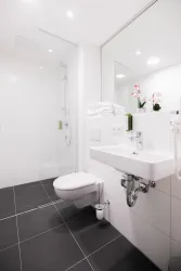 Ein modernes Badezimmer mit einer Dusche, einem Waschbecken und einer Toilette. Weiße Wände und schwarze Fliesen schaffen eine elegante Atmosphäre.