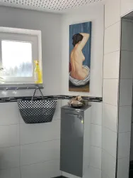 Ein modernes Badezimmer mit hellen Fliesen und einer Fensteraussicht. An der Wand hängt ein Gemälde einer sitzenden Figur.