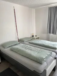 Ein helles Schlafzimmer mit zwei Einzelbetten. Die Bettwäsche ist grün mit Punkten und es gibt einen kleinen Tisch neben den Betten.