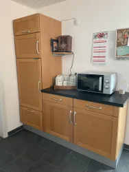 Eine moderne Küche mit einem Kühlschrank, einer Mikrowelle und Holzschränken. Die Arbeitsfläche ist schwarz und abwechslungsreich gestaltet.