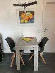 Ein Tisch mit zwei schwarzen Stühlen in einer modernen Küche. Über dem Tisch hängt eine Lampe, und an der Wand hängt ein stilllebenartiges Bild von Obst.