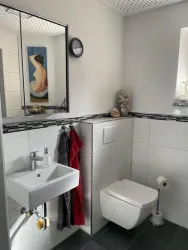 Ein modernes Badezimmer mit einer Wandfärbung in Weiß und schwarzer Bordüre. Es gibt ein Waschbecken, eine Toilette und ein Kunstwerk an der Wand.
