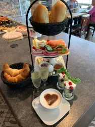 Ein liebevoll angerichtetes Frühstück mit Brötchen, Croissants, frischem Obst, Aufschnitt und Joghurt. Dazu gibt es Kaffee und Sekt in Gläsern.