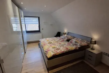 Ein modernes Schlafzimmer mit einem großen Bett und bunten Bettdecken. Es gibt eine Fenstersicht und eine stilvolle Schlafzimmermöbelkombination.