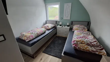Ein gemütliches Schlafzimmer mit zwei Einzelbetten und bunten Bettdecken. Es gibt einen modernen Nachttisch und ein Fenster mit Blick nach draußen.