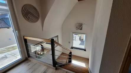 Eine helle Treppe mit moderner Geländer und Holzdetails. Der Raum hat große Fenster, die viel Licht hereinlassen.