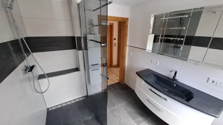 Ein modernes Badezimmer mit einer gläsernen Dusche und einem eleganten Waschbecken. Die Wände sind mit hellen und dunklen Fliesen gestaltet.