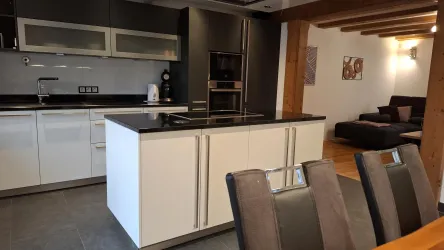 Moderne Küche mit einer eleganten Kücheninsel und schwarzer Arbeitsfläche. Im Hintergrund ist ein gemütlicher Wohnbereich sichtbar.
