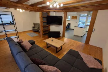 Ein gemütliches Wohnzimmer mit einer modernen Couch und einem Holztisch. Der Raum hat schöne Holzbalken und viel natürliches Licht.