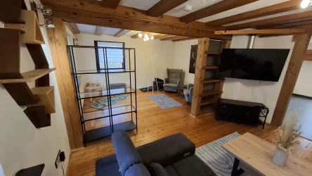 Ein gemütliches Wohnzimmer mit Holzvertäfelung und moderner Einrichtung. Eine Sitzgruppe, ein TV und Bücherregale schaffen eine einladende Atmosphäre.