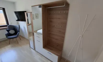 Ein modern gestalteter Raum mit einem Kleiderschrank und einem Spiegel. In der Ecke steht ein bequemer Sessel und der Boden ist aus hellem Holz.