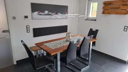 Ein moderner Essbereich mit einem Holzertisch und schwarzen Stühlen. Die Wände sind schlicht und es gibt ein dekoratives Bild im Hintergrund.