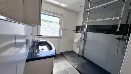 Ein modernes Badezimmer mit einer großen Dusche und einer eleganten Waschbeckenzeile. Helle Fliesen und viel natürlichem Licht durch das Fenster schaffen eine angenehme Atmosphäre.