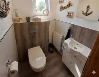 Ein modernes Badezimmer mit einer Toilette und einem Waschbecken. Die Wände sind hell und es gibt nautische Dekorationen.