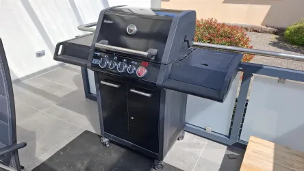 Ein schwarzer Gasgrill steht auf einer modernen Terrasse. Die Umgebung ist hell und freundlich gestaltet.