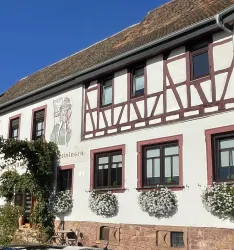 Ein historisches Fachwerkhaus mit bunten Fensterrahmen. Blumenkästen schmücken die Fenster und die Fassade strahlt Gemütlichkeit aus.