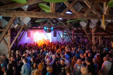 Eine lebhafte Nachtveranstaltung in einem stilvollen Veranstaltungsort. Die Menge tanzt und genießt die Musik unter bunten Lichtern.