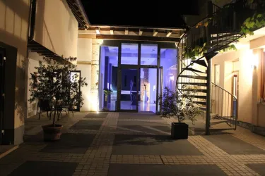 Ein einladender Innenhof mit modernen Elementen, der von Pflanzen umgeben ist. Im Hintergrund leuchtet ein blauer Raum, der eine angenehme Atmosphäre schafft.