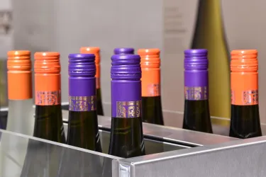 Eine Reihe von Flaschen mit bunten Verschlüssen, darunter lila und orange. Die Flaschen stehen in einem Metallregal.