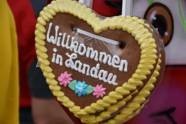 Ein herzförmiger Lebkuchen mit der Aufschrift „Willkommen in Landau“. Er ist mit bunten Verzierungen und Zuckerguss dekoriert.