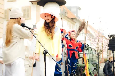 Eine fröhliche Faschingsfeier mit Menschen in bunten Kostümen. Im Vordergrund stehen zwei Frauen, die miteinander sprechen und eine bunte Atmosphäre schaffen.