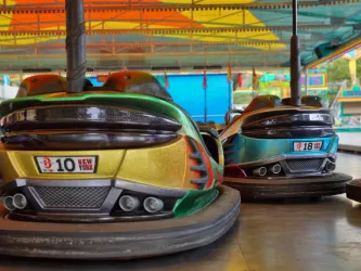 Bumper Cars auf einem Jahrmarkt unter einem bunten Zelt. Die Fahrzeuge haben auffällige Farben und Nummernschilder.