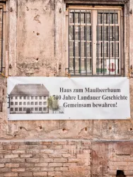 Ein Banner an einer Mauer informiert über das "Haus zum Maulbeerbaum" und feiert 700 Jahre Landauer Geschichte. Es ruft dazu auf, gemeinsam die Geschichte zu bewahren.