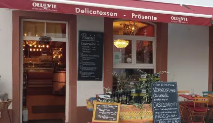 Ein einladendes Delikatessengeschäft mit einem roten Schild und einer Auswahl an italienischen Produkten. Vor der Tür steht ein Tisch mit frisch verpackten Lebensmitteln und einem Menü.