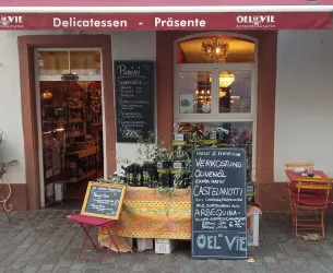 Ein charmantes Delikatessengeschäft mit einem einladenden Eingangsbereich. Auf einem Tisch stehen Olivenölflaschen und eine Tafel mit Angeboten.