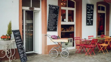 Ein gemütliches Café mit Tischen und Stühlen im Freien. Die Wände sind mit Tafeln beschriftet, die die Speisen und Getränke auflisten.