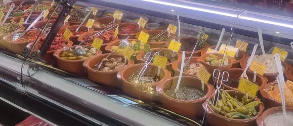 Eine Vielzahl von kleinen Töpfen mit verschiedenen Speisen ist in einem Verkaufsregal angeordnet. Jede Speise ist mit einem Etikett versehen.