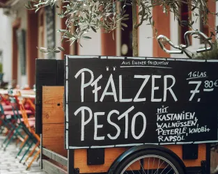 Ein Holzstand mit einer Tafel, auf der "Pfälzer Pesto" steht. Das Pesto kostet 7,80 € und enthält Kastanien, Walnüsse, Petersilie, Knoblauch und Rapsöl.