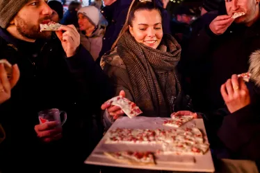 Eine Gruppe von Menschen genießt Essen auf einem festlichen Markt. Eine Frau lächelt, während sie ein Stück Essen hält und sich mit anderen unterhält.