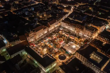 Ein festlich beleuchteter Weihnachtsmarkt in der Stadt bei Nacht. Stände und Lichter schaffen eine einladende Atmosphäre.