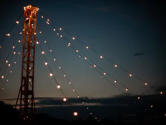 Ein hoher Mast mit Lichtern leuchtet in der Dämmerung. Der Himmel ist dunkelblau mit einigen Wolken.