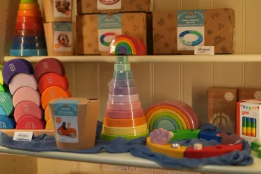 Eine Auswahl an bunten Spielzeugen steht auf einem Regal. Darunter befinden sich Stapelspielzeuge, Regenbögen und andere bunte Lernspielzeuge.