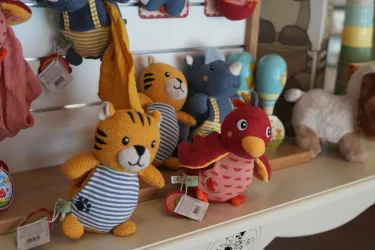 Eine Reihe von bunten Stofftieren steht auf einem Regal. Darunter sind ein gestreifter Tiger und ein roter Vogel zu sehen.