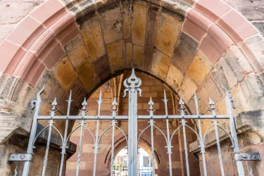 Ein historisches Tor mit einem schmiedeeisernen Gitter und einem Halbkreis. Der Steinbogen ist gut erhalten und zeigt eindruckvolle Details.