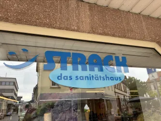 Ein Geschäft mit dem Namen "STRACH das sanitäthaus" ist abgebildet. Das Schild ist blau und gut sichtbar.