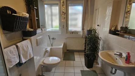 Ein sauberes Badezimmer mit Toilette, Waschbecken und großen Fenstern. Grüne Pflanzen und Handtücher sorgen für eine einladende Atmosphäre.