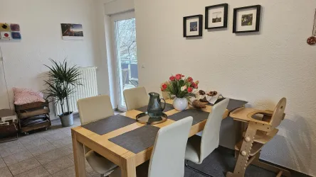 Ein einladender Essbereich mit einem Holztisch und weißen Stühlen. Auf dem Tisch stehen ein Blumenstrauß und dekorative Gegenstände.