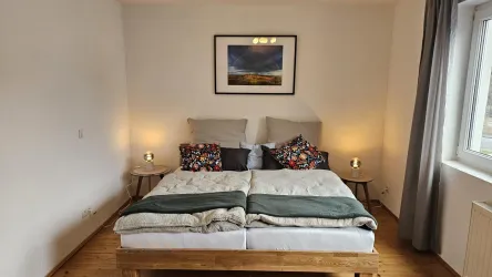 Ein gemütliches Schlafzimmer mit einem Doppelbett und bunten Kissen. Sanftes Licht von den Nachttischlampen schafft eine einladende Atmosphäre.