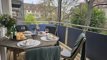 Ein gemütlicher Balkon mit einem Tisch, der für ein Abendessen gedeckt ist. Kerzen, Glasrotwein und frische Blumen verleihen der Szene eine einladende Atmosphäre.