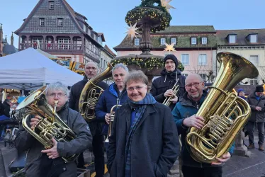 Eine Gruppe von Musikern steht in der Stadt und spielt Tuba. Im Hintergrund sind festliche Dekorationen und historische Gebäude zu sehen.