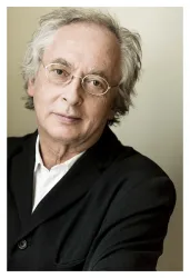 Ein Mann mit grauen Haaren und Brille trägt einen schwarzen Blazer. Er schaut in die Kamera und hat einen nachdenklichen Gesichtsausdruck.