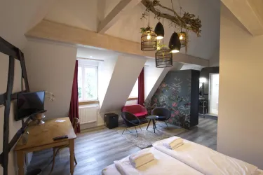 Ein modernes Zimmer mit zwei Betten, einem stilvollen Tisch und einem Fernseher. Die Wände sind hell und es gibt eine kreative Blumendekoration im Hintergrund.