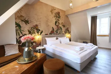 Ein helles und modernes Zimmer mit einem großen Bett und stilvoller Dekoration. Die Wand ist mit einem floralen Muster gestaltet, das eine warme Atmosphäre schafft.