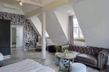 Ein modernes Schlafzimmer mit schrägen Wänden und einem gemütlichen Sofa. Der Raum ist hell und einladend, mit Fenster, die natürliches Licht hereinlassen.